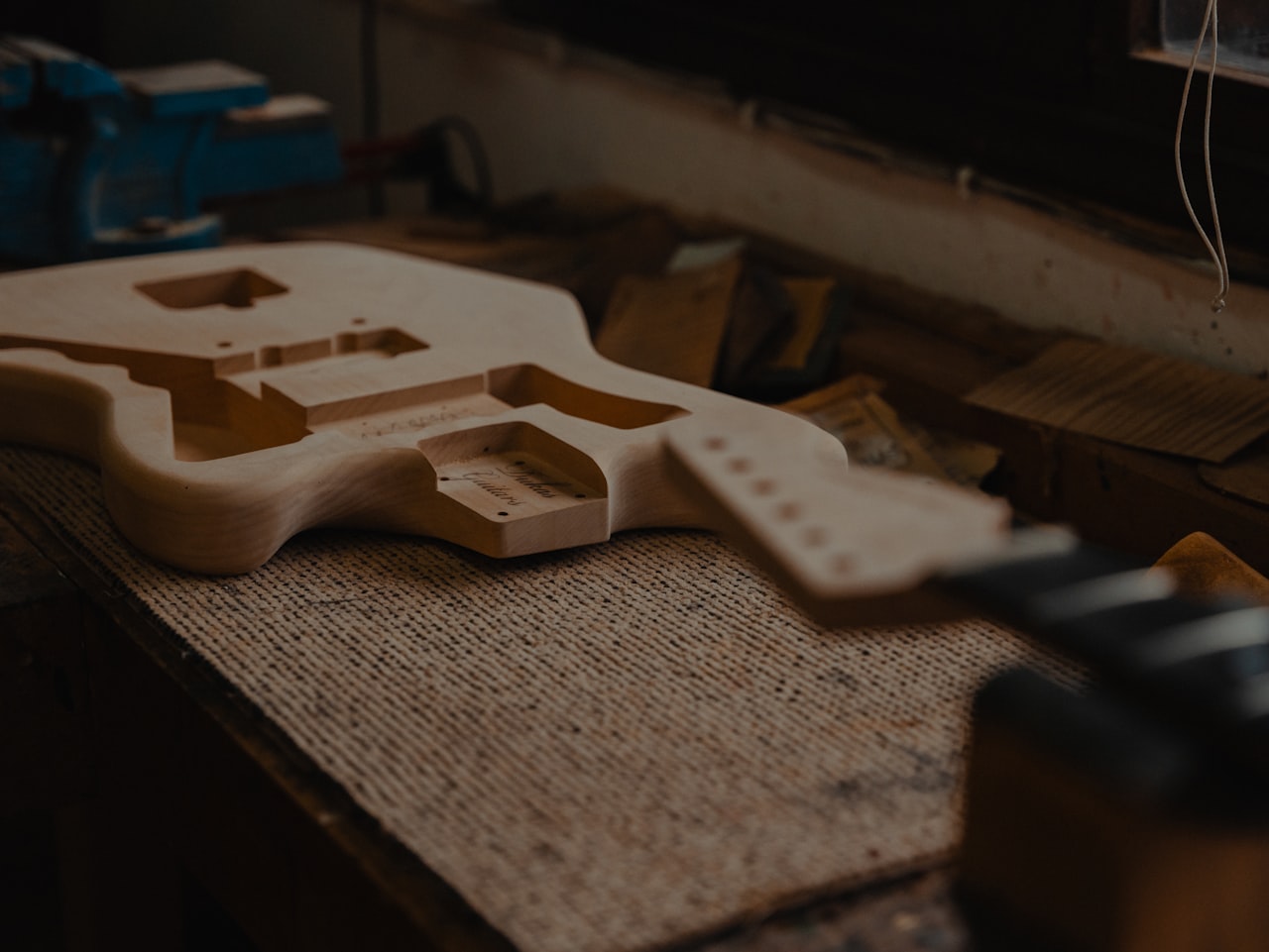 Manos de luthier trabajando en el cuerpo de una guitarra sobre el banco del taller