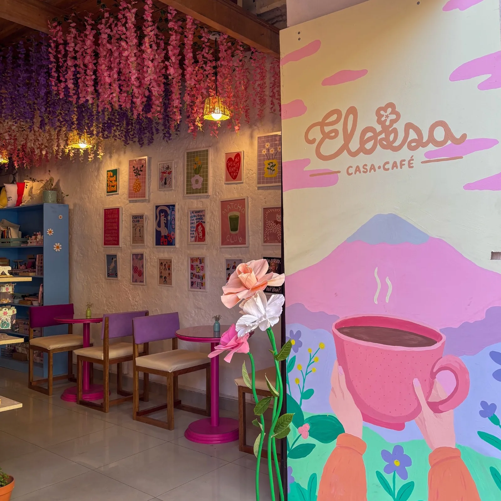 Interior de Eloísa Casa Café: el mural pintado a mano, las glicinas colgantes y la pared de láminas