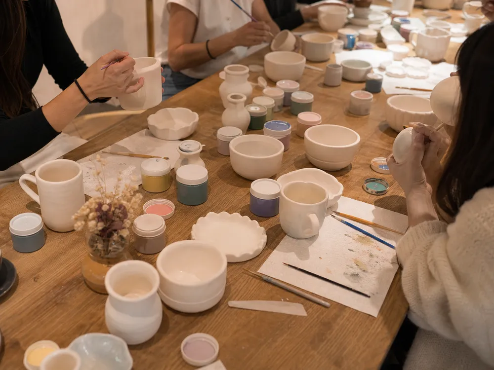 Mesa larga del taller con piezas de cerámica sin pintar y pinturas
