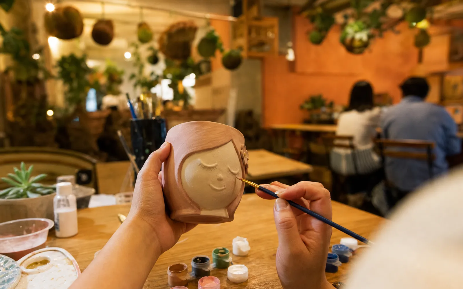 Manos pintando una maceta de cerámica en el taller